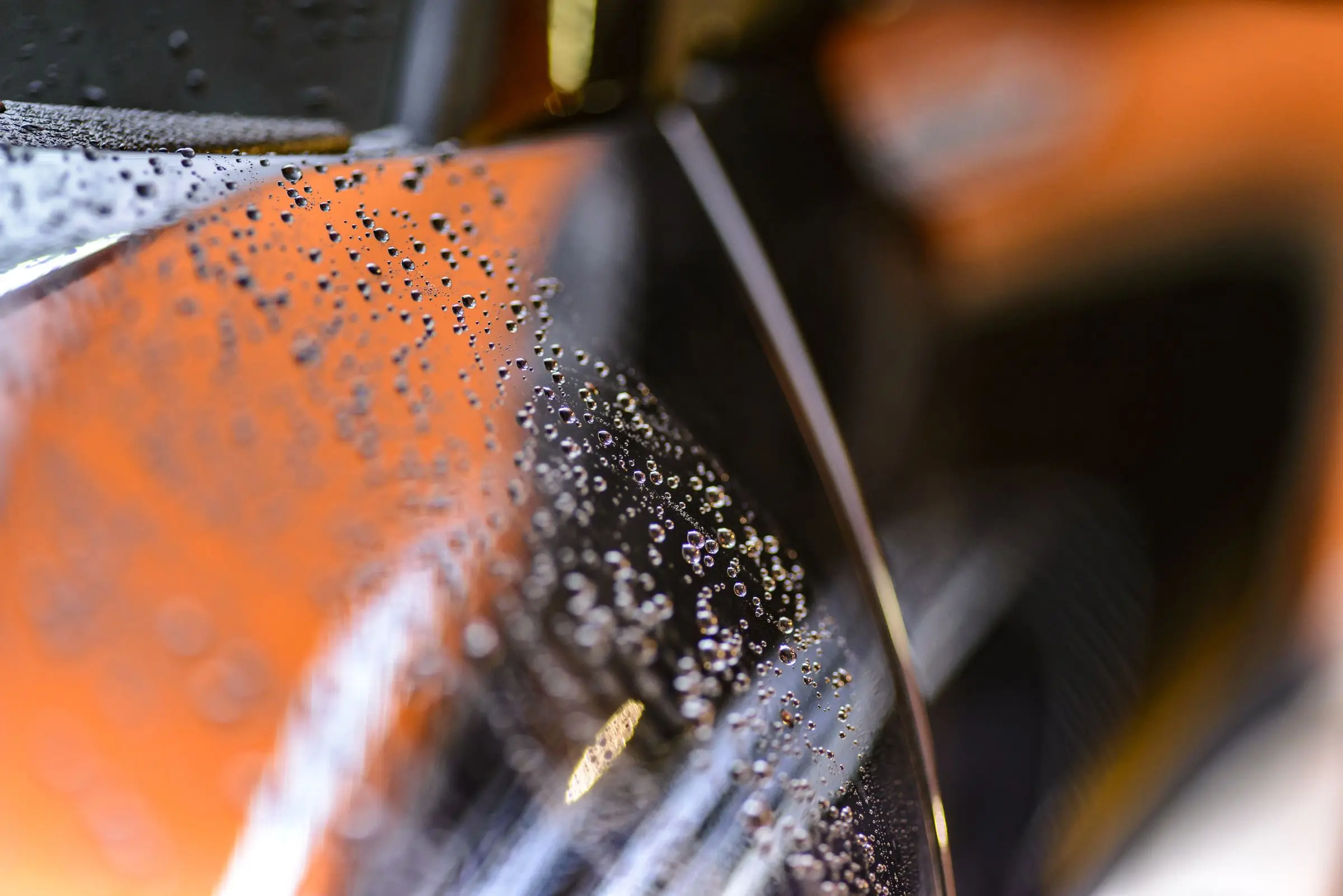 Water droplets beading tightly on a glossy car panel, the background thrown out of focus behind them.