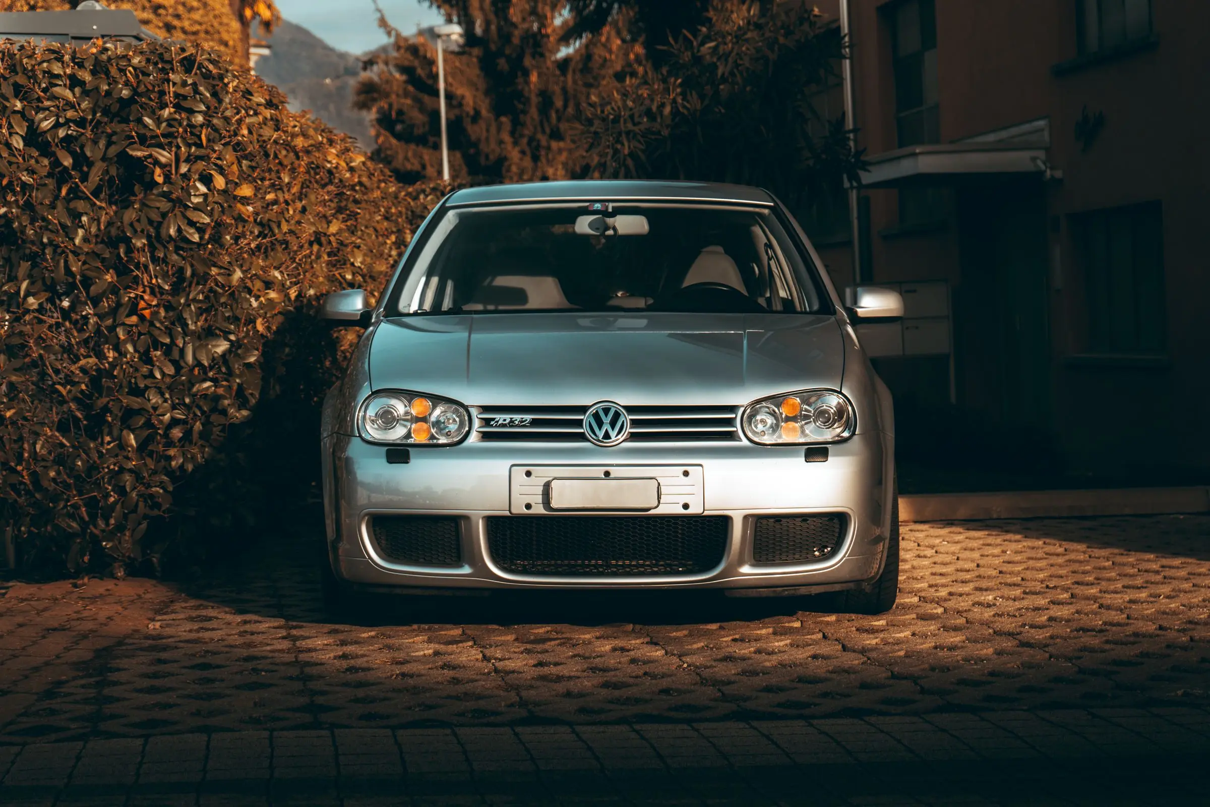 A silver hatchback parked in low, warm sunlight beside a hedge, the light raking across its bonnet.