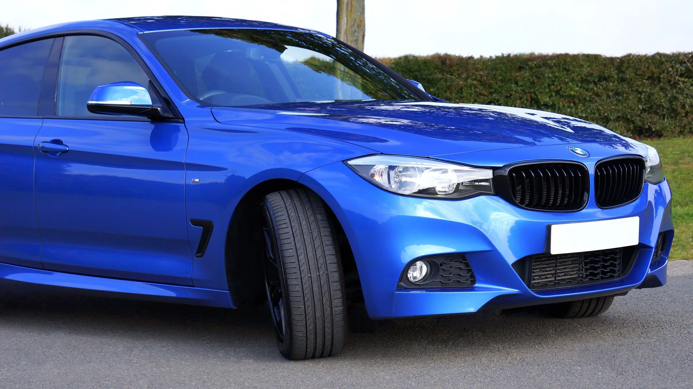 A freshly cleaned blue sedan parked outdoors, its paint reflecting the sky above it.