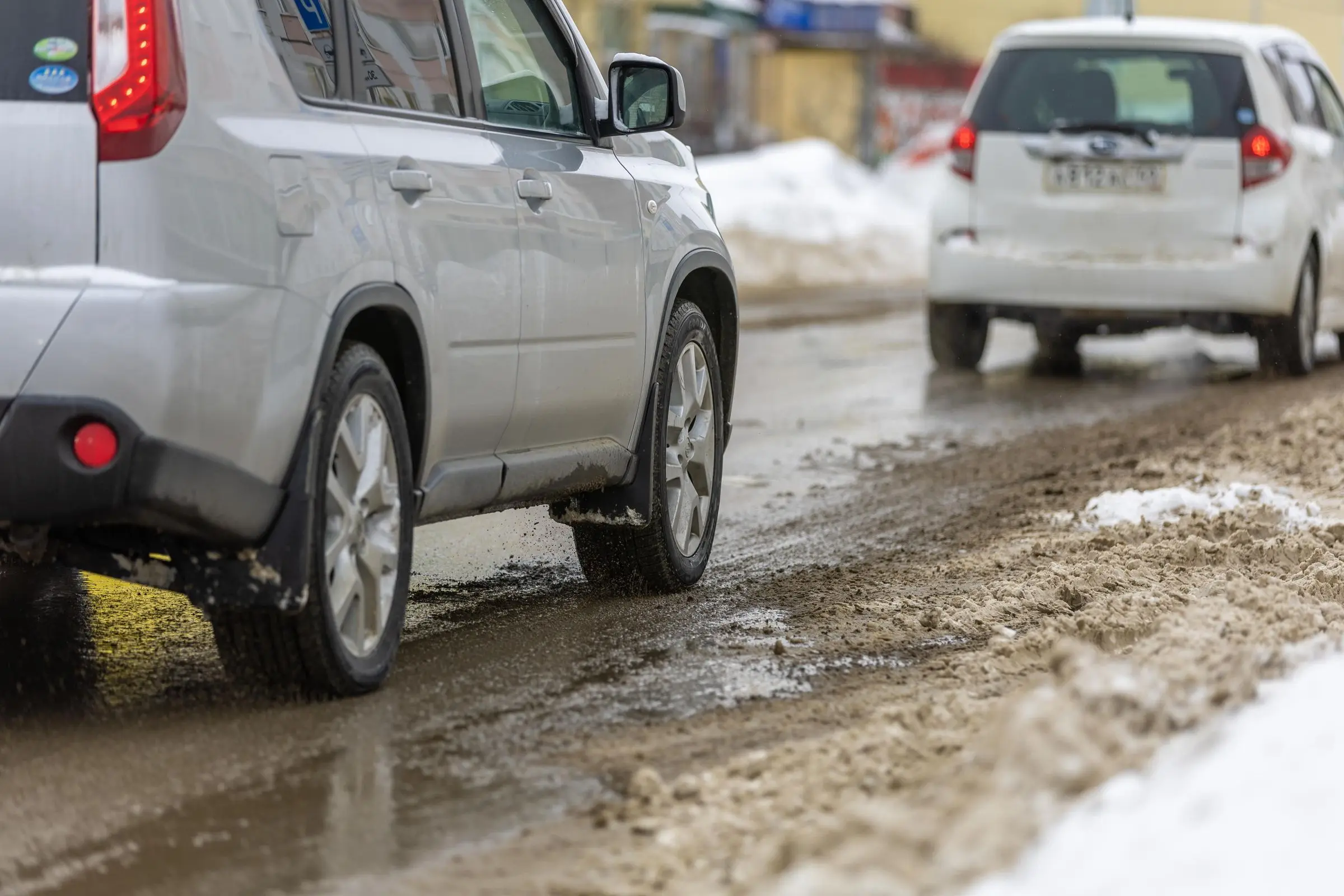 Cars driving on a wet, slush-covered winter street, brine and grit sprayed across their lower panels.