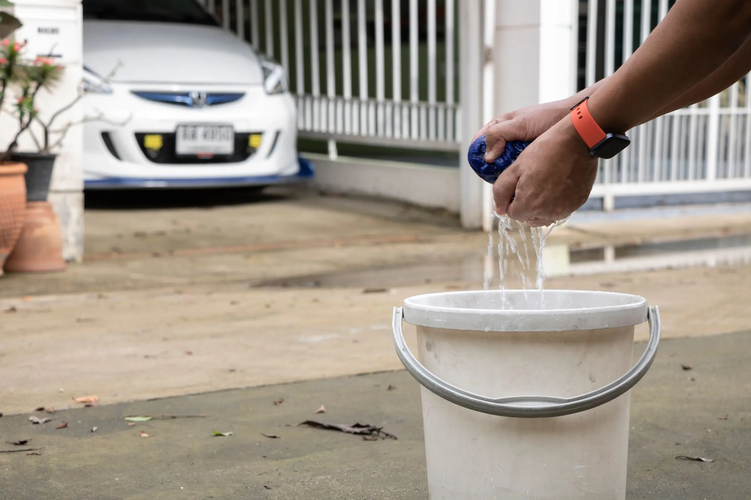 A car being washed by hand with a sponge and bucket on a residential driveway.
