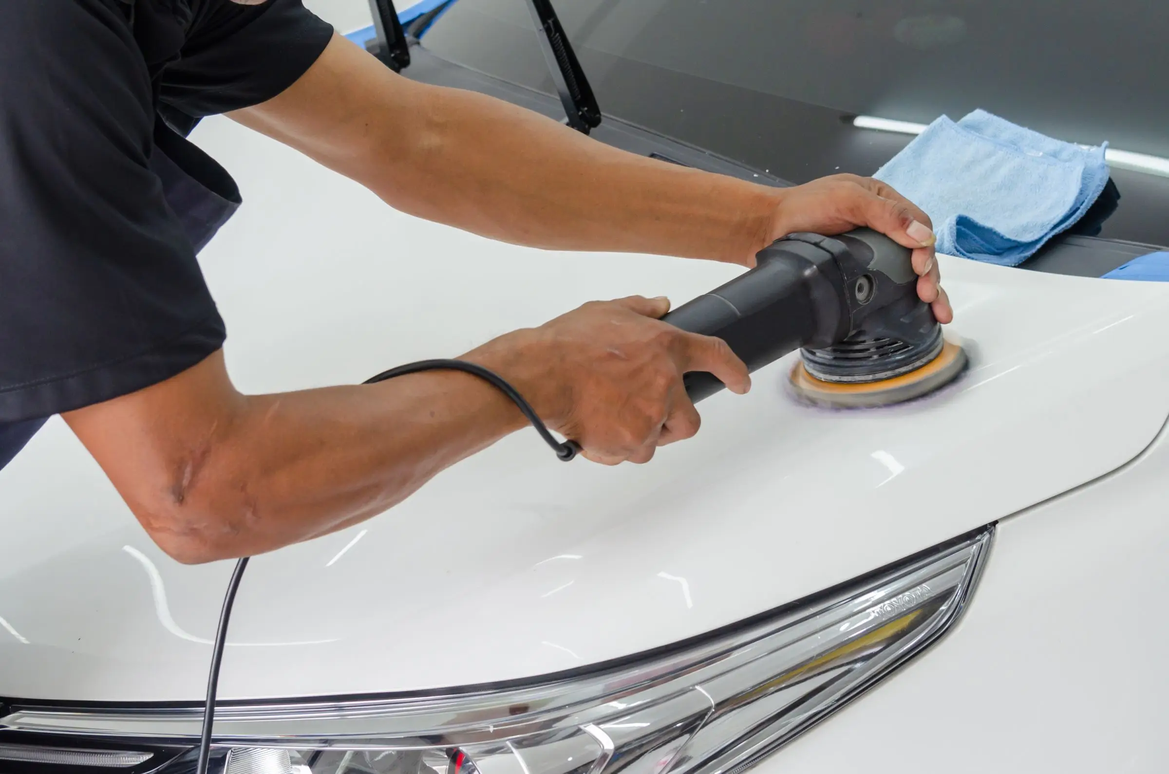 A detailer running a rotary polisher across a white car bonnet during paint preparation.