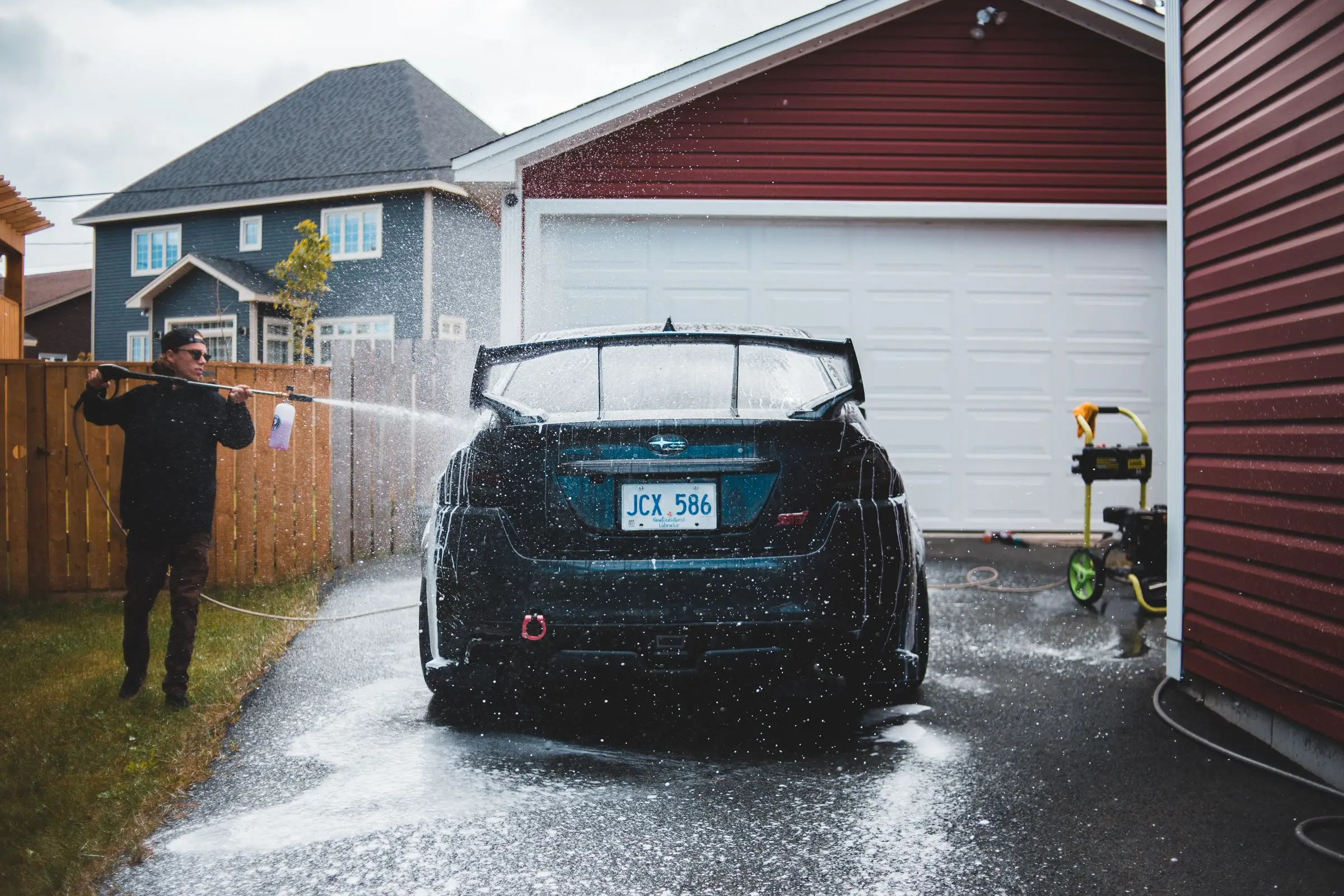 Someone rinsing a car down with a hose outdoors, water sheeting off the panels.