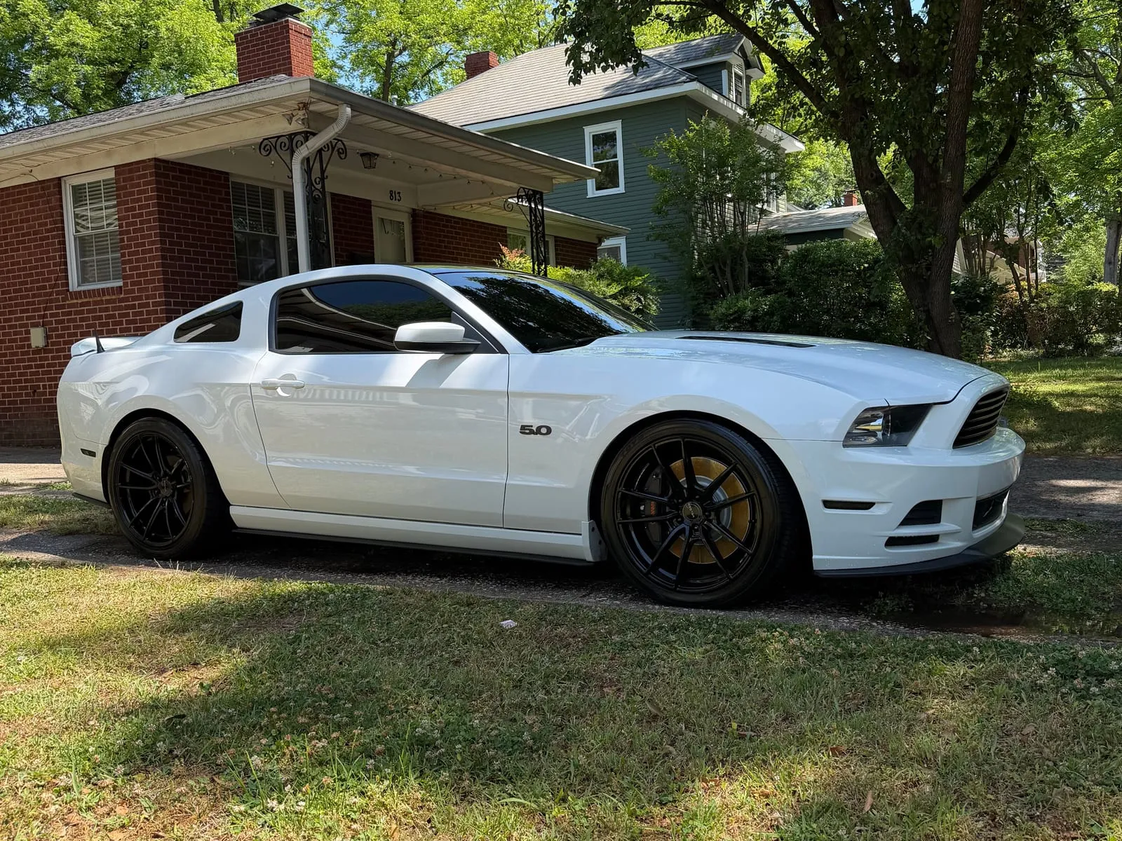 A white Ford Mustang parked on a lawn beside a brick house after a full detail